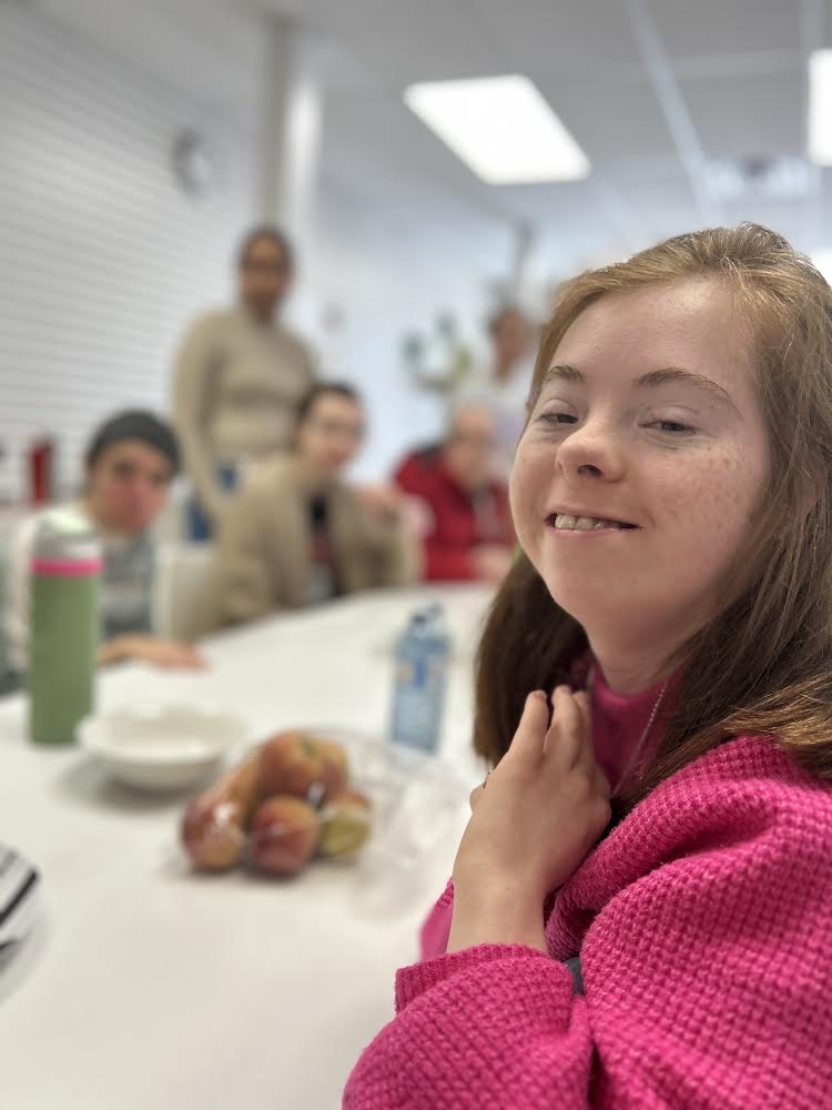 A member smiles over lunch with friends at the Cambridge day program.