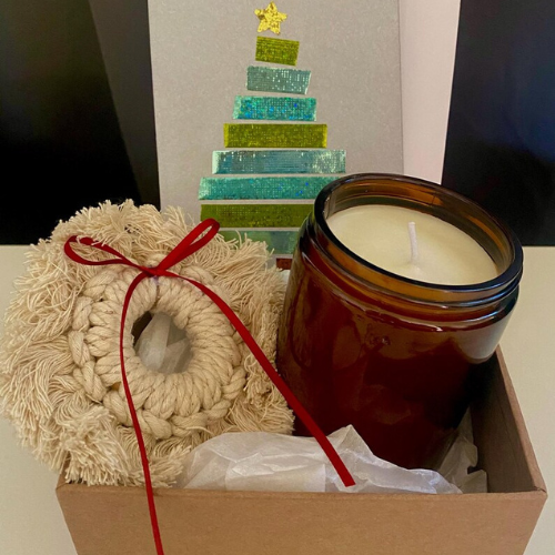 A curated gift box holding a hand-poured candle and a hand-knotted macramé wreath